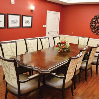 A formal dining room with a long wooden table and elegant chairs, surrounded by artwork and warm red walls.