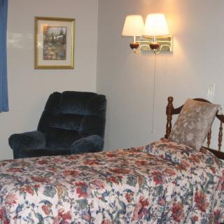 A cozy bedroom with floral bedding, an armchair, and wall lamp.