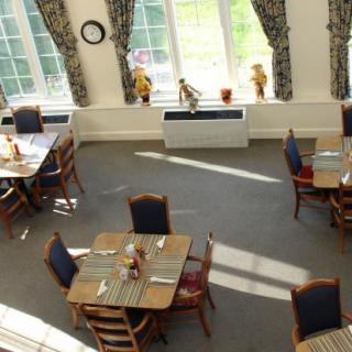 An empty dining room with neatly arranged tables and chairs, illuminated by sunlight through large windows.