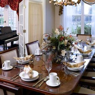 An elegantly set dining room table with a floral centerpiece and a view of a piano in the background.