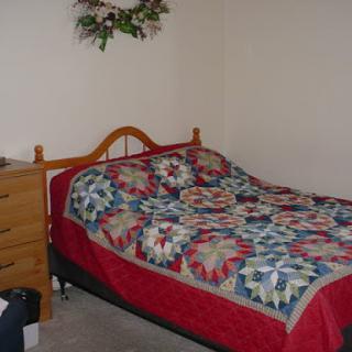 A cozy bedroom featuring a wooden bed with a colorful quilt and a chest of drawers.