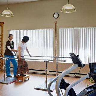 A physical therapy session with a patient using parallel bars for support.