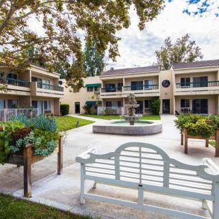A peaceful courtyard featuring a central fountain and a bench surrounded by landscaped greenery and residential buildings.