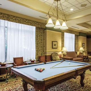 A cozy billiard room featuring a pool table with lighting fixtures overhead and comfortable seating around.