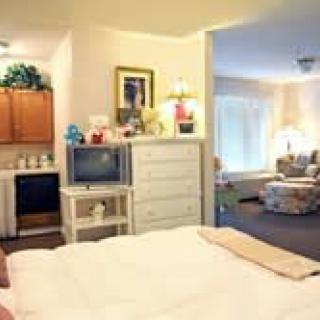 A cozy bedroom with a dresser, television, and a view into an adjoining living room.