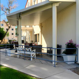 A cozy outdoor patio with furniture under an awning, surrounded by potted plants and railings.