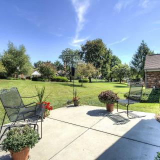 A sunny patio overlooking a spacious green lawn with outdoor furniture and potted plants.