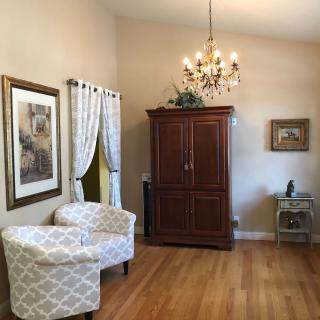 A cozy living room with two patterned armchairs, a wooden cabinet, a chandelier, and hardwood flooring.