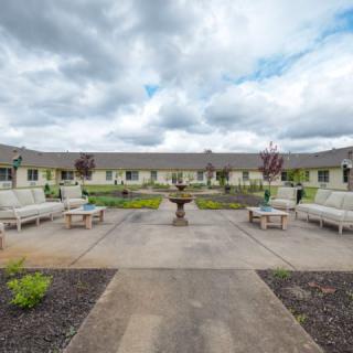 A serene courtyard featuring benches, a central fountain, and manicured landscaping under a cloudy sky.