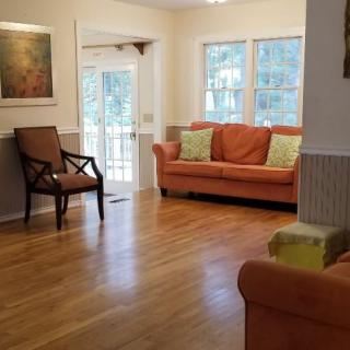 A cozy living room with a sofa and armchair, featuring hardwood floors and natural light from large windows.