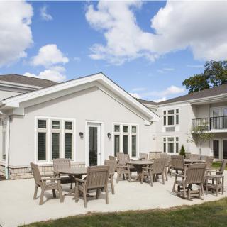 A spacious outdoor patio area with tables and chairs against a modern building backdrop under a partly cloudy sky.