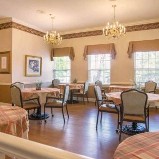 A well-lit dining room with elegantly set tables and chairs, featuring large windows and chandeliers.