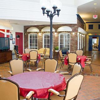 A cozy indoor dining area with round tables, comfortable chairs, and a brick wall backdrop.