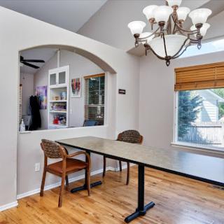 A cozy dining area featuring a modern chandelier, a long table with chairs, and ample natural light from the window.