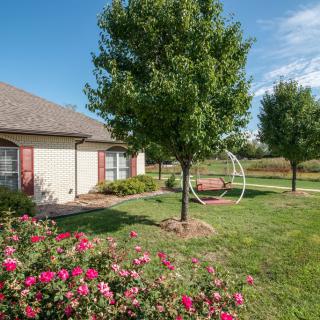 A beautifully landscaped yard with a house, trees, flowers, and a swing on a sunny day.