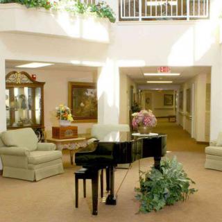 A spacious lobby featuring a grand piano and comfortable seating, surrounded by natural light and decorative plants.