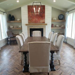 A well-decorated dining room with a large wooden table, upholstered chairs, and a central fireplace.