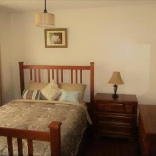 A cozy bedroom featuring a wooden bed frame, bedside table, and soft lighting.