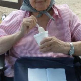 An elderly person enjoying ice cream outdoors while seated in a wheelchair.
