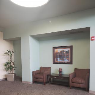 A small lobby area featuring two chairs, a table with decorative items, a painting on the wall, and a potted plant.
