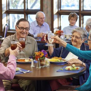 A group of seniors enjoying a meal together and toasting in a dining setting.