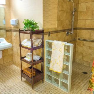 A bathroom with organized shelves holding towels and a small plant, featuring tiled walls and floor.