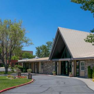 A modern building with a triangular roof, surrounded by trees and a paved driveway under a clear blue sky.
