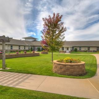 A scenic view of a building with a well-maintained lawn, trees, and clear pathways under a cloudy sky.