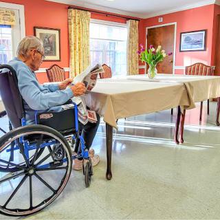 An elderly person sitting in a wheelchair, engrossed in reading inside a care facility.