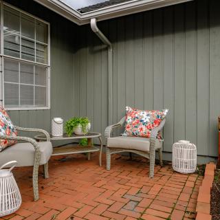 Cozy patio area with brick flooring and outdoor seating, featuring colorful pillows and decorative plants.
