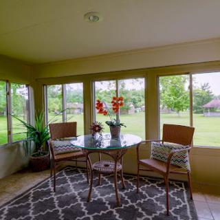 A cozy sunroom featuring a glass table and seating, surrounded by large windows that let in plenty of natural light.