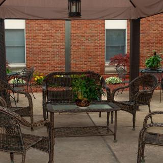 A cozy patio area featuring wicker furniture and potted plants against a brick wall backdrop.