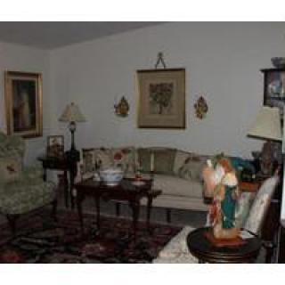 A cozy living room with traditional decor, featuring a sofa, armchair, and various artworks on the walls.