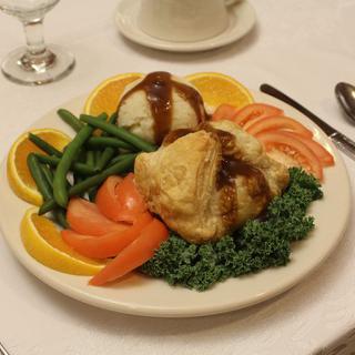 A plated dinner featuring roasted chicken, mashed potatoes topped with gravy, green beans, sliced tomatoes, and orange slices garnished with parsley.