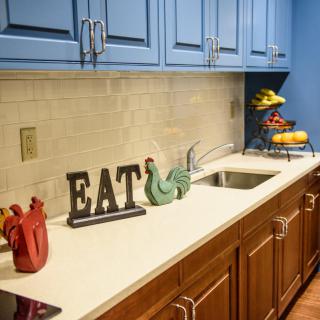 A stylish kitchen with blue upper cabinets, a clean white countertop, and decorative elements including a fruit stand.
