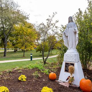 A statue surrounded by autumn decorations, including pumpkins and flowers, in a scenic park setting.