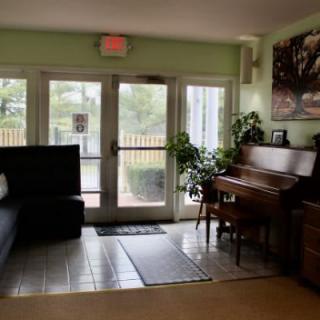A cozy lobby area featuring a piano, sofa, and plants near large glass doors.