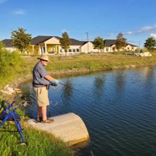 A man enjoying fishing by the lakeside near residential houses.