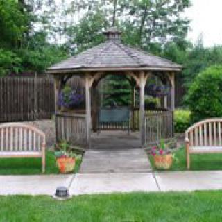 A quaint wooden gazebo surrounded by greenery with benches and potted plants.