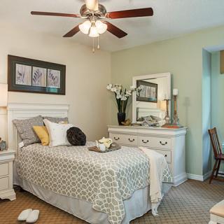 A cozy bedroom with a single bed, decorated with a neutral color palette and featuring a ceiling fan.