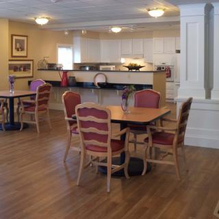 A cozy dining area with wooden tables and chairs, featuring warm lighting and a buffet counter in the background.