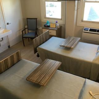 A well-lit hospital room featuring two patient beds and a chair, designed for comfort and care.