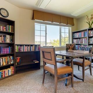 A cozy library reading room with bookshelves, a table, and chairs by a large window.