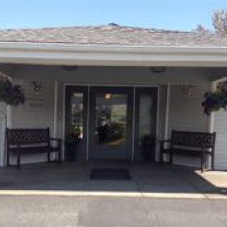 An entrance to a building flanked by benches and hanging flower pots on a sunny day.