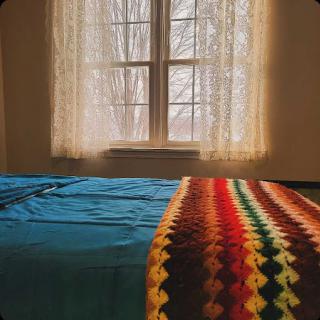 A cozy bedroom with a view, featuring a colorful blanket draped over the bed and warm natural light filtering through the window.