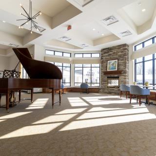 A spacious and well-lit lounge featuring a grand piano, large windows, and a cozy fireplace.