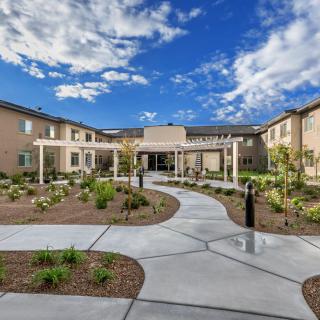 A modern building with a landscaped garden and pathway under a bright blue sky with clouds.