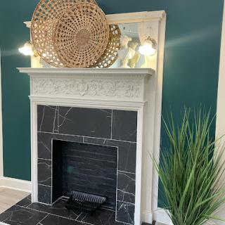 A beautifully styled modern fireplace with a striking green wall backdrop, featuring decorative elements and a touch of greenery.