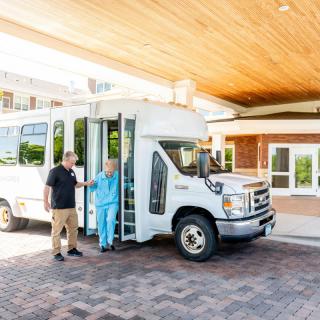 A shuttle bus parked at the entrance of a building, with people exiting.
