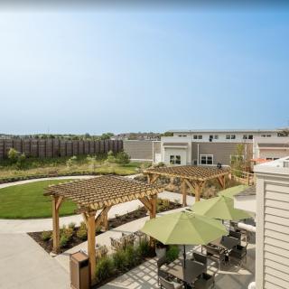 A sunny outdoor courtyard with pergolas, a green lawn, and seating areas.